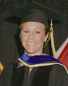 A graduate in a black cap and gown with a blue and gold hood smiles at the camera.