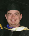 A person is smiling and wearing a graduation cap and gown.